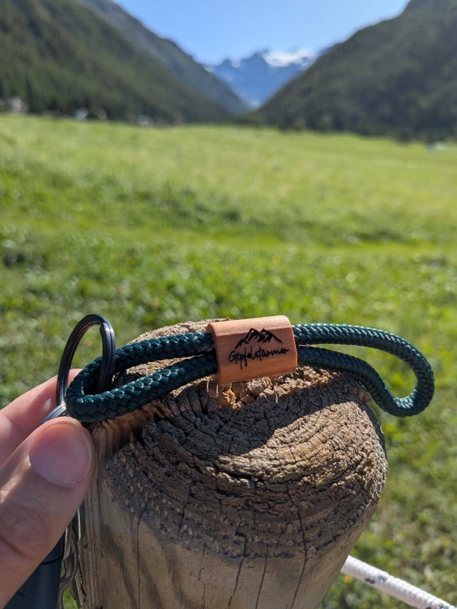 Der Schlüsselanhänger mit Bergrelief liegt vor beeindruckendem Bergpanorama in der Sonne. 