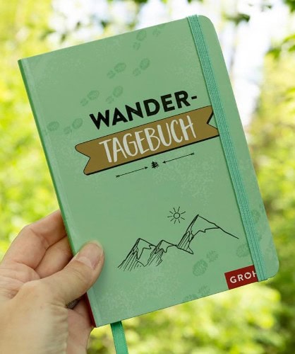 Linda hält ein grünes Wandertagebuch in der Hand. Ein hervorragendes Geschenk für Wanderer, die ihre Touren lieber analog als digital festhalten.