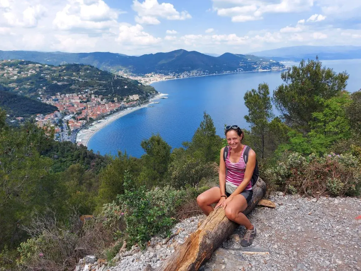 Linda sitzt an einem Aussichtspunkt mit Blick auf die Palmenriviera, die Küste von Noli vom Capo Noli aus