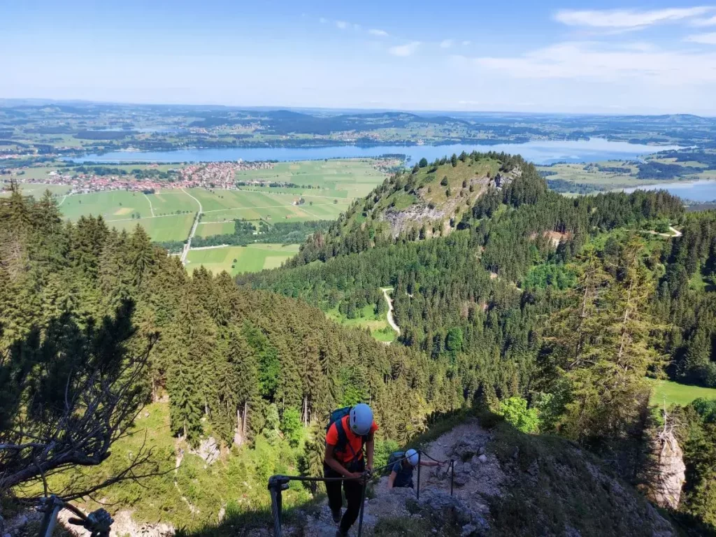 Zwei Klettersteig-Teilnehmer steigen über Drahtseile und Leitern an der Gelben Wand empor. Dieser Einsteigerklettersteig zeigt die Vielfalt des Tegelbergs bei Füssen.