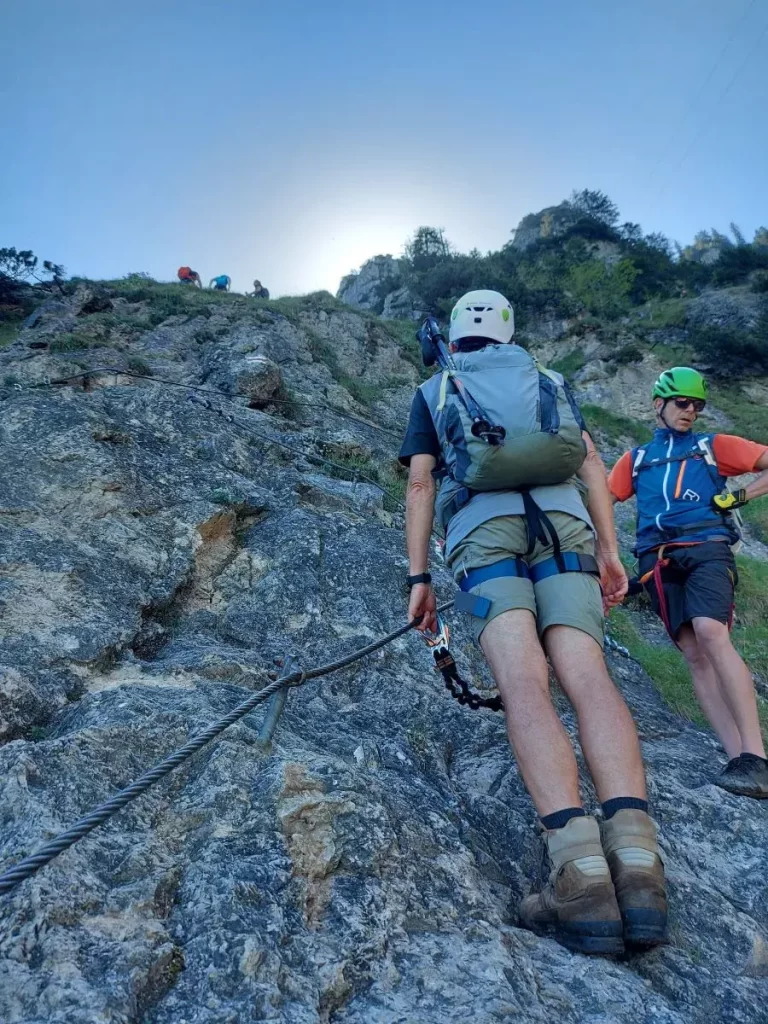 Zwei Kletterer sichern sich mit Karabinern am Fels und blicken zu weiteren Steig-Abschnitten. Dieser Ausschnitt veranschaulicht die abwechslungsreichen Kletterpassagen neben der Wanderroute am Tegelberg von Füssen.