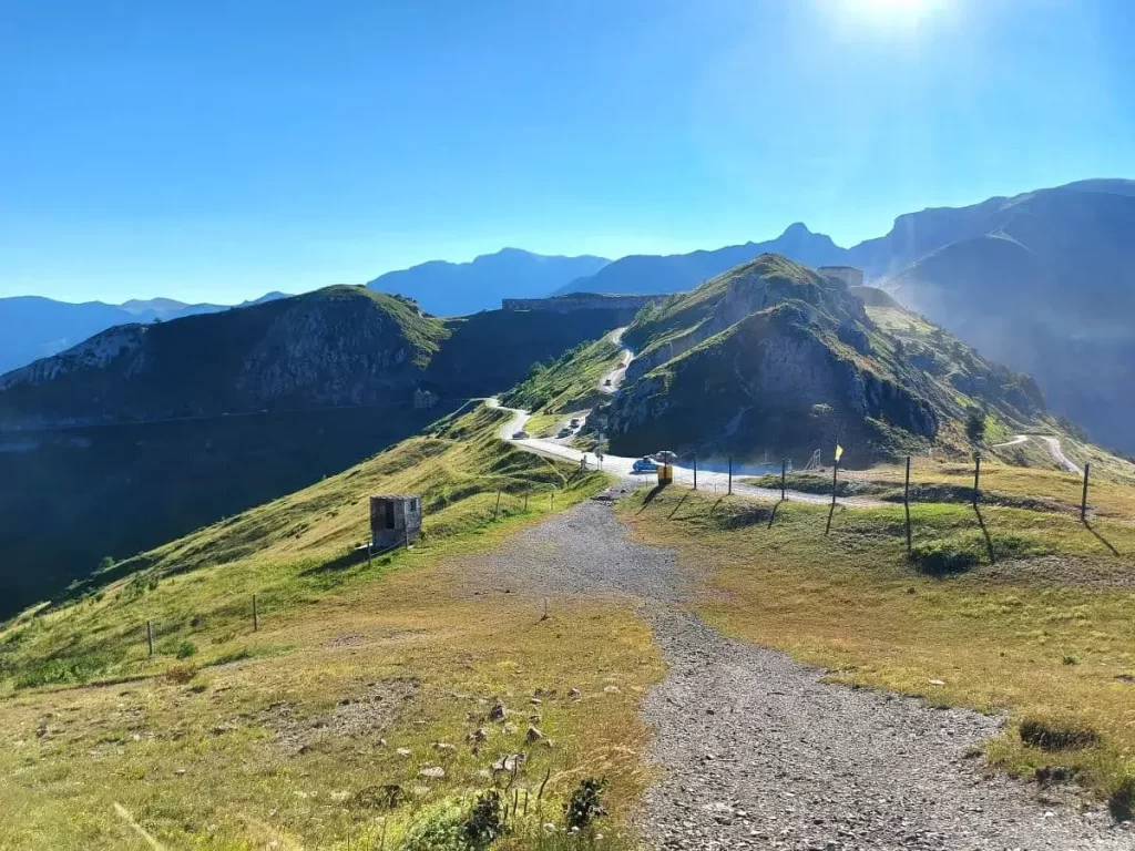 Ausblick auf den Colle di Tenda und die kurvige Straße, die als Südrampe ins Roya-Tal führt. Die Strecke ist von grünen Hügeln und felsigen Gipfeln umgeben und lädt zu einer landschaftlich reizvollen Fahrt ein.