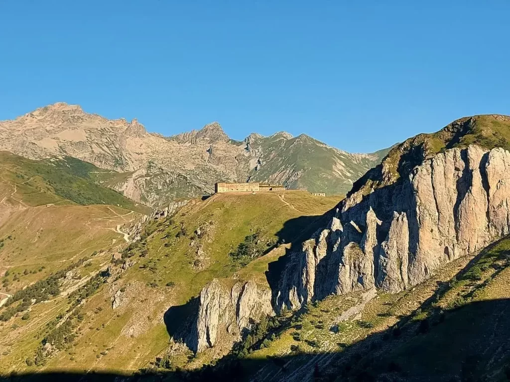 Blick auf das durch die Abendsonne angestrahlte Forte Centrale auf dem Colle di Tenda. Dahinter erheben sich die mächtigen Berggipfel der Seealpen.