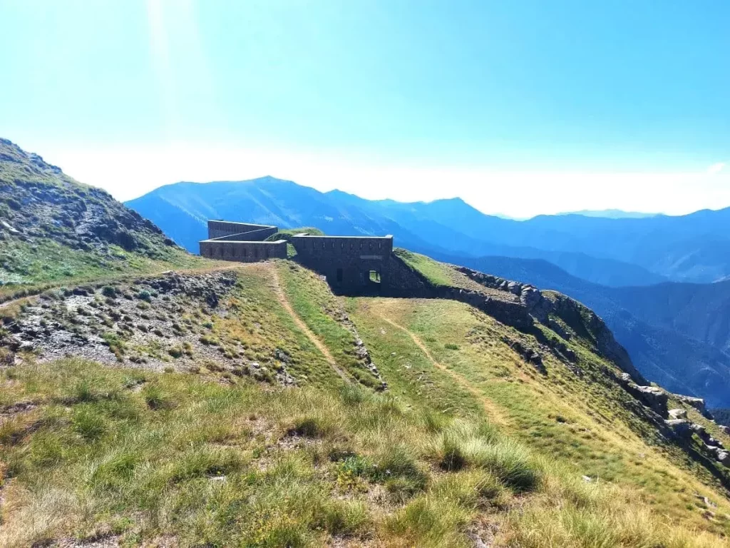 Ein verlassenes Fort aus Stein liegt ruhig auf einer Anhöhe und bietet einen weiten Blick auf die umliegenden Täler. Die dicken Mauern und das verwitterte Gestein zeugen von der Geschichte und Widerstandskraft des Gebäudes. Im Hintergrund erstreckt sich die sanfte Berglandschaft unter einem blauen Himmel, der die Atmosphäre friedlich und erhaben wirken lässt.
