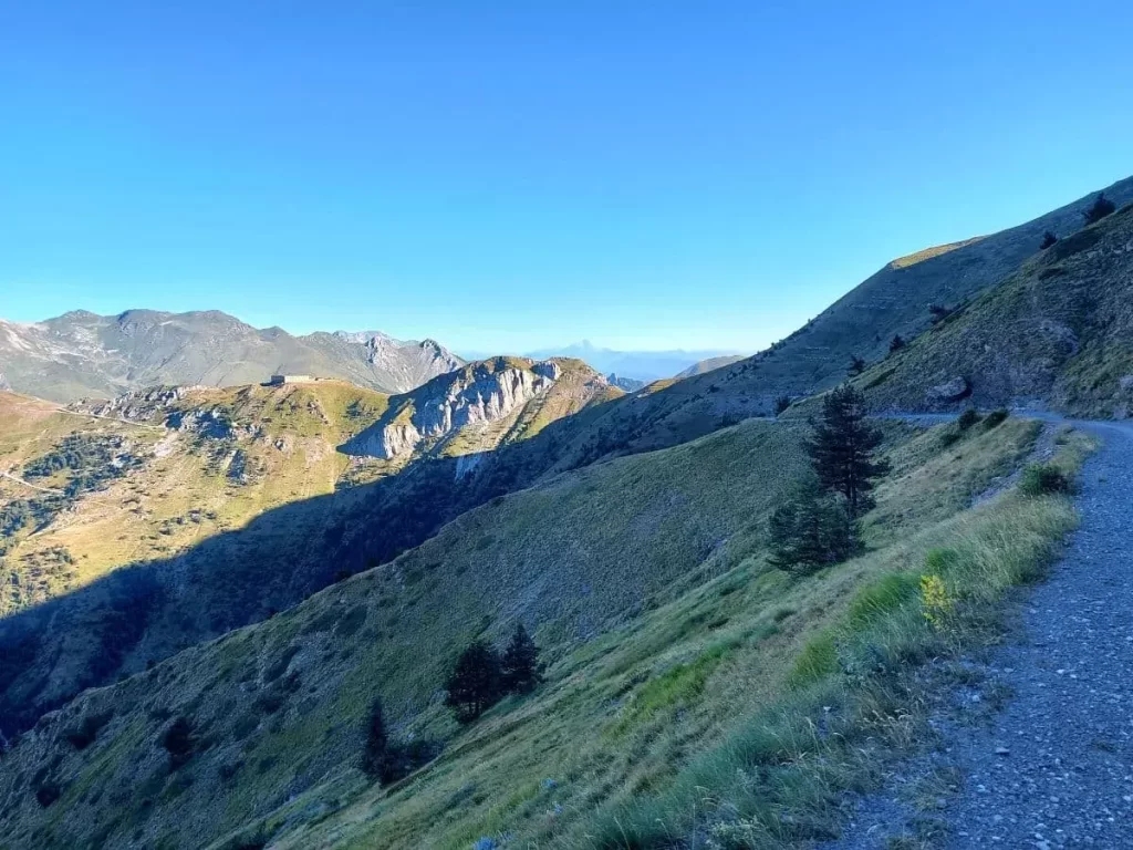 Ein schmaler Wanderweg führt über saftig grüne Wiesen und entlang eines steinigen Berghangs vom Colle di Tenda zum Fort Tabourde. Der Weg schlängelt sich durch die alpine Landschaft und gibt weite Ausblicke auf die umliegenden Täler frei. Die klare Bergluft und die abwechslungsreiche Natur verleihen dem Pfad eine idyllische Atmosphäre.
