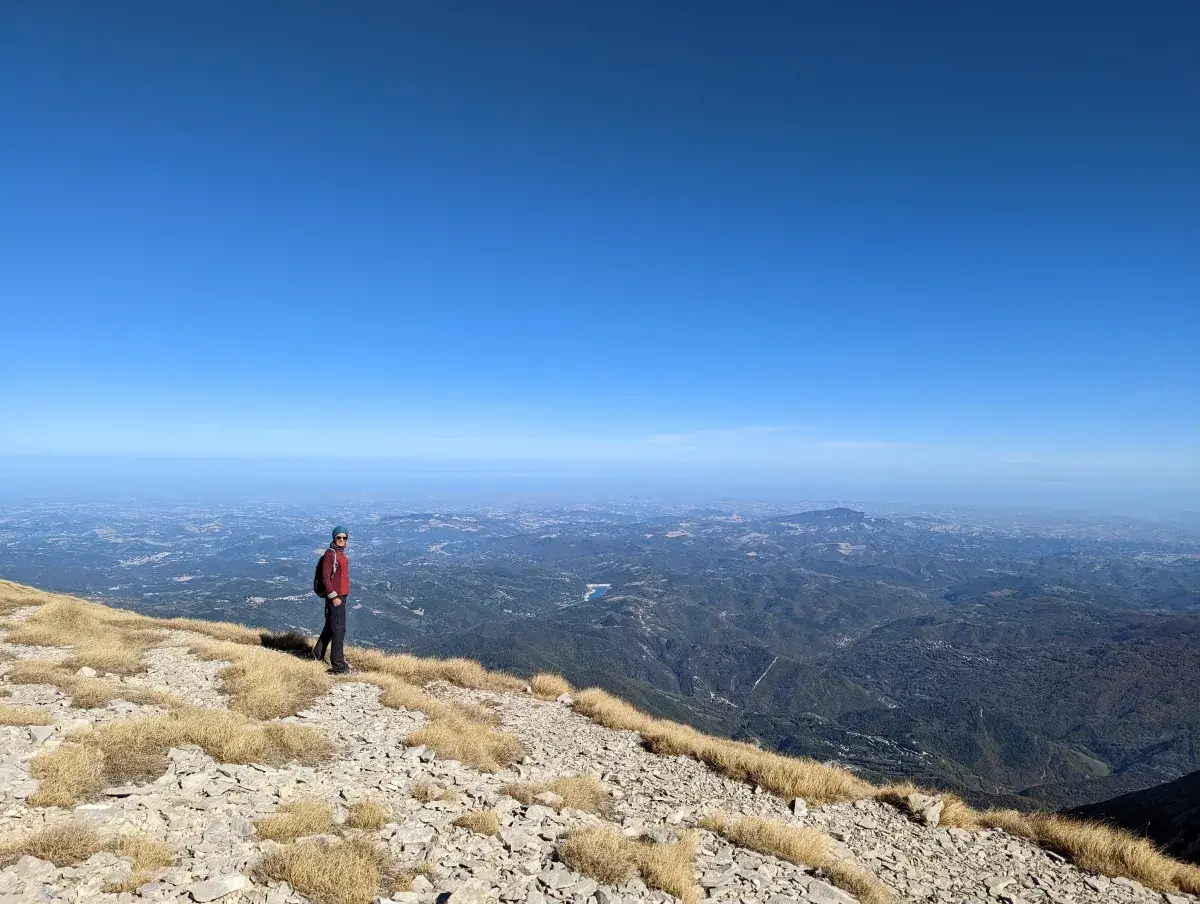 Linda steht auf einem Berggipfel des Monti Sibillini Nationalpark und blickt auf die italienische Stadt Ancona sowie die Küstenlinie hinunter, die weit in der Ferne zu sehen ist.