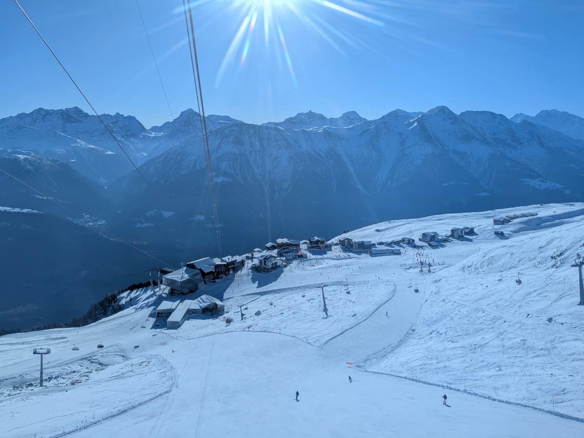 Mehrere Skifahrer sind auf breiten, sonnigen Pisten der Fiescheralp unterwegs, umgeben von schneebedeckten Gebäuden und markanten Gipfeln der Walliser Alpen. Die Höhenlage und das weite Panorama machen die autofreie Fiescheralp im Wallis zu einem beliebten Ziel für Wintersportler.