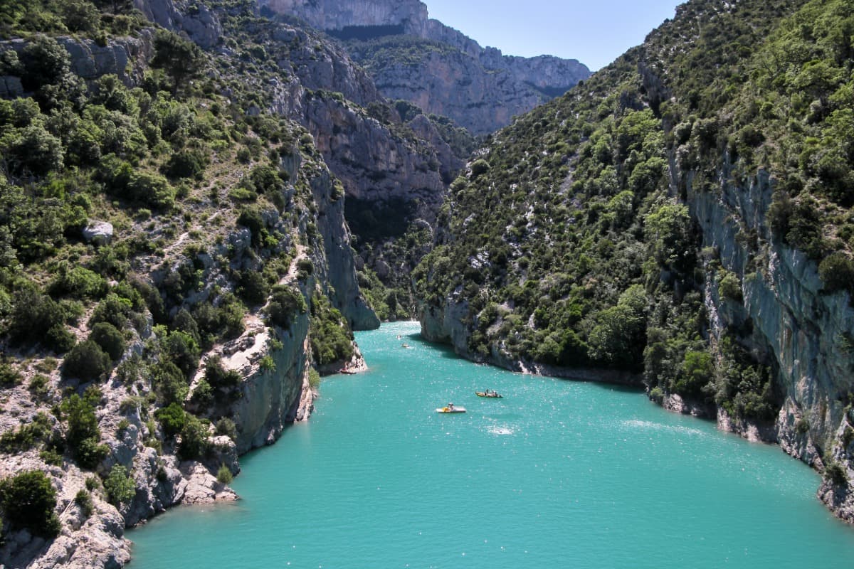 Tief eingeschnittene Schlucht mit türkisblauem Wasser, eingerahmt von steilen, bewaldeten Felswänden – die Verdon-Schlucht in Südfrankreich. Mehrere kleine Boote und Kanus gleiten durch das klare Wasser unter strahlend blauem Himmel.