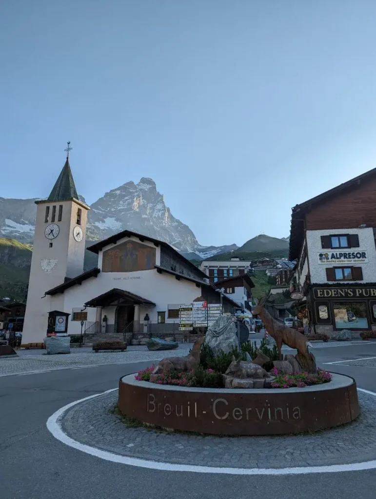 Der Dorfplatz von Breuil-Cervinia mit Kirche, Brunnen und Blick auf die umliegenden Alpen vermittelt alpines Flair. Dieser Ort am Fuß des Matterhorns ist ein beliebter Ausgangspunkt für Wanderungen und Sehenswürdigkeiten im Aostatal.