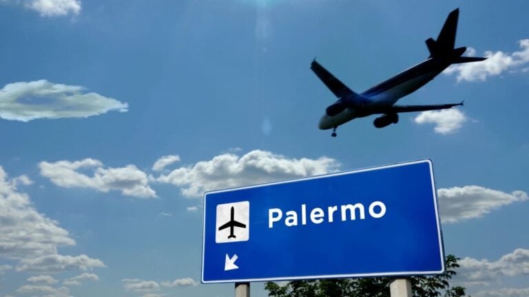 Ein Flugzeug fliegt über ein Straßenschild mit der Aufschrift „Palermo“ und einem Flugzeugsymbol – eine passende Illustration für einen Urlaubskostenrechner, der die Anreise nach Sizilien per Flugzeug berücksichtigt.