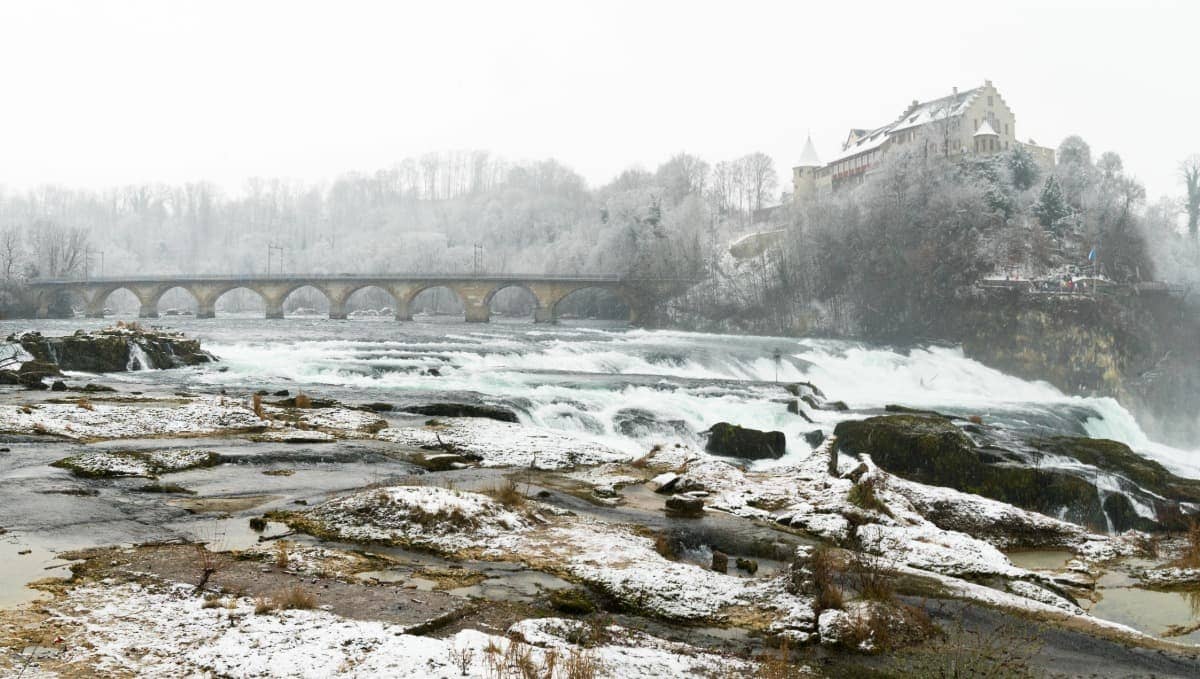 Verschneite Landschaft rund um den berühmten Rheinfall. Diese mystische Landschaft macht den Wasserfall zu einem beliebten Ausflugsziel im Winter.
