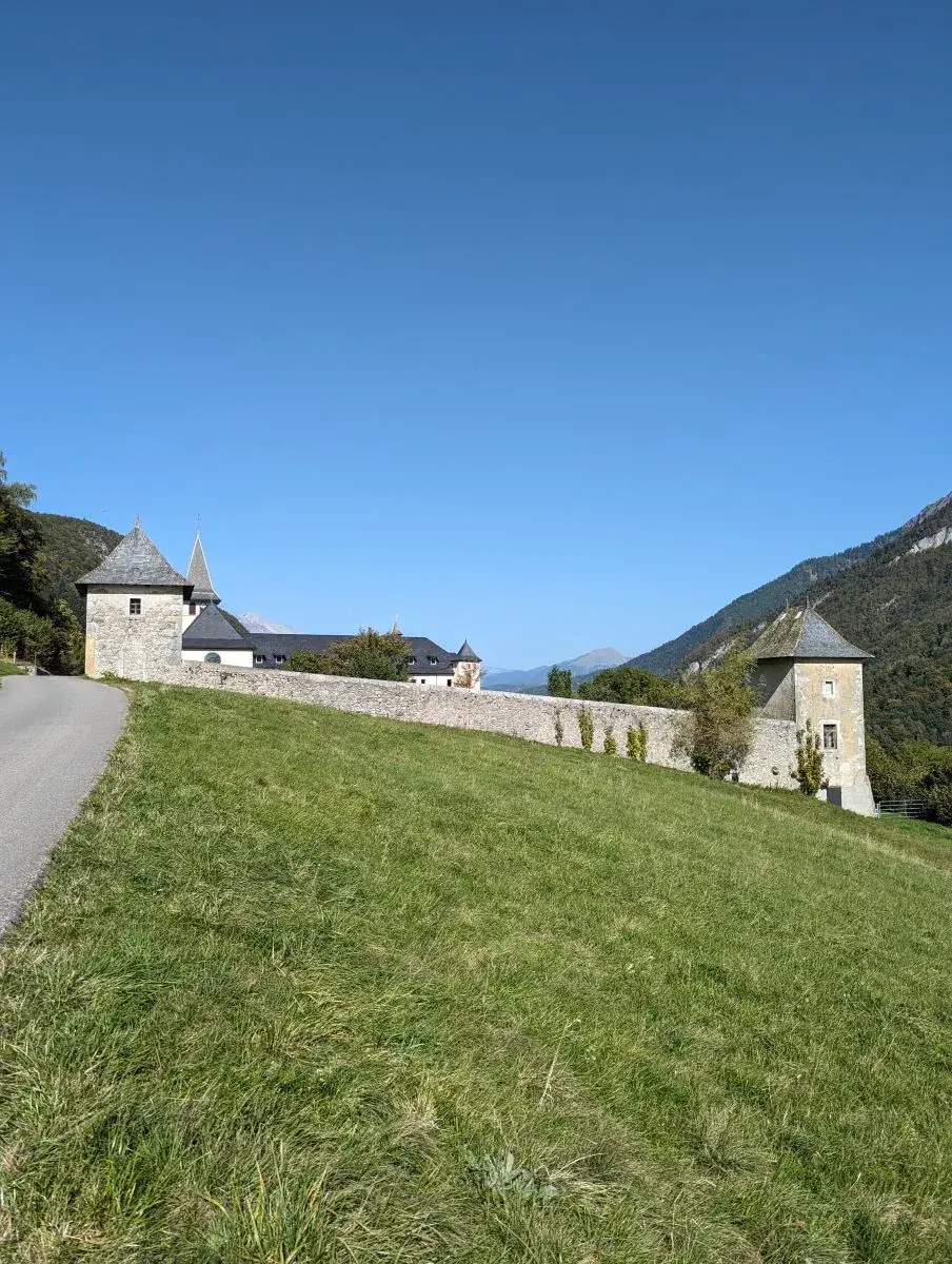 Das von dicken Mauern umschlossene Kloster Tamié auf einer grünen Wiese und Berge im Hintergrund