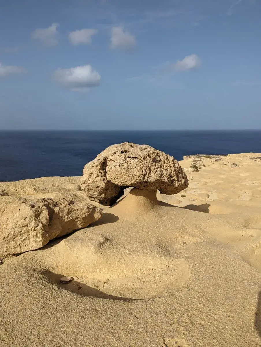 Eine natürlich geformte Kalksteinformation an der golden, leuchtenden Küste Gozos, unter einem klaren, wolkenverhangenen Himmel, mit Blick auf das ruhige Mittelmeer.