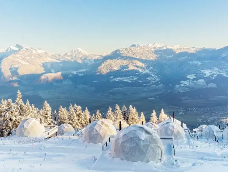 Mehrere Whitepods, ganz besondere Unterkünfte der Schweiz, blicken in Richtng der verschneiten Alpen