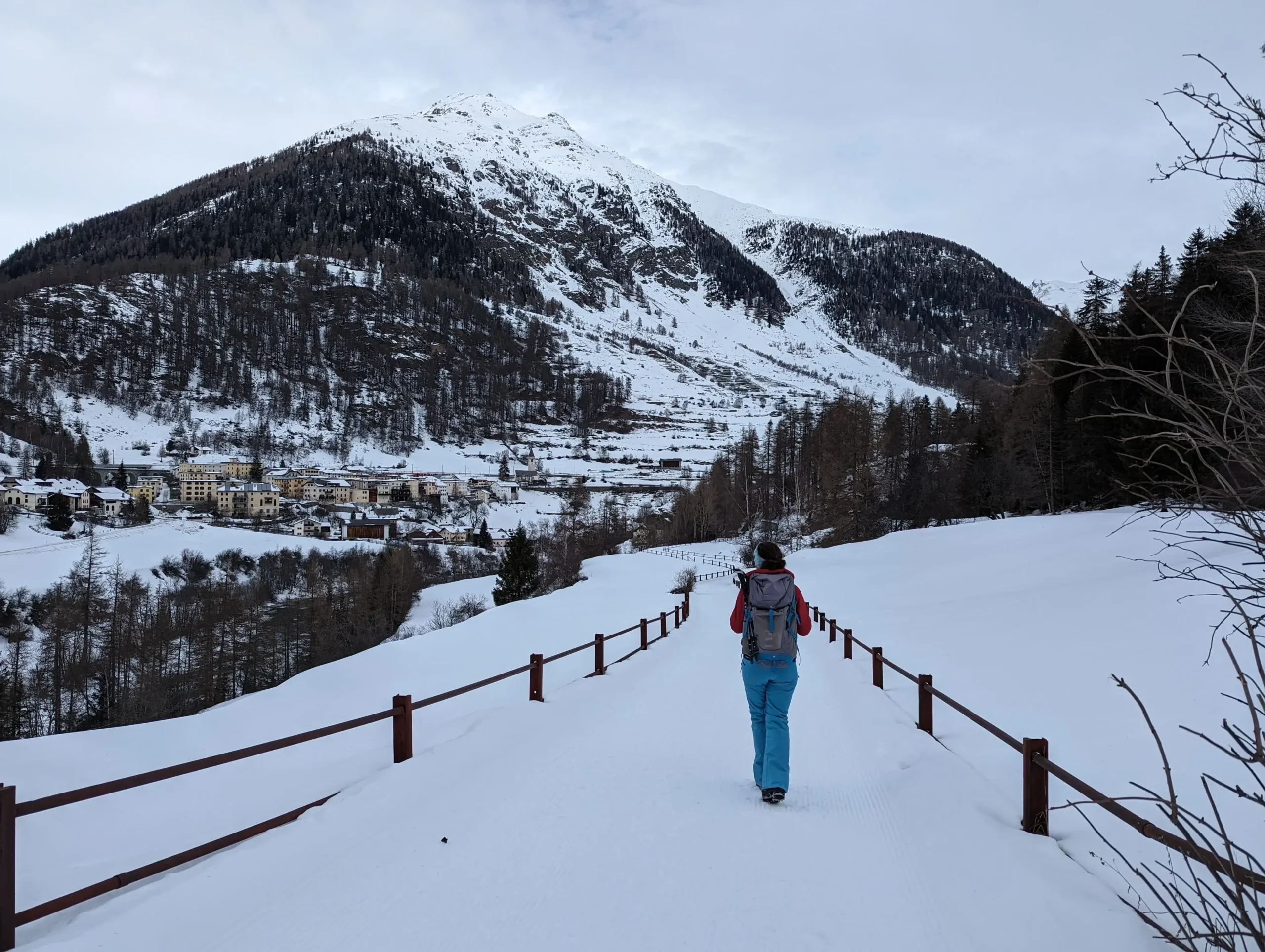 Linda wandert auf dem Winterwanderweg Via Engiadina auf das Bergdorf Lavin zu, das im Tal liegt