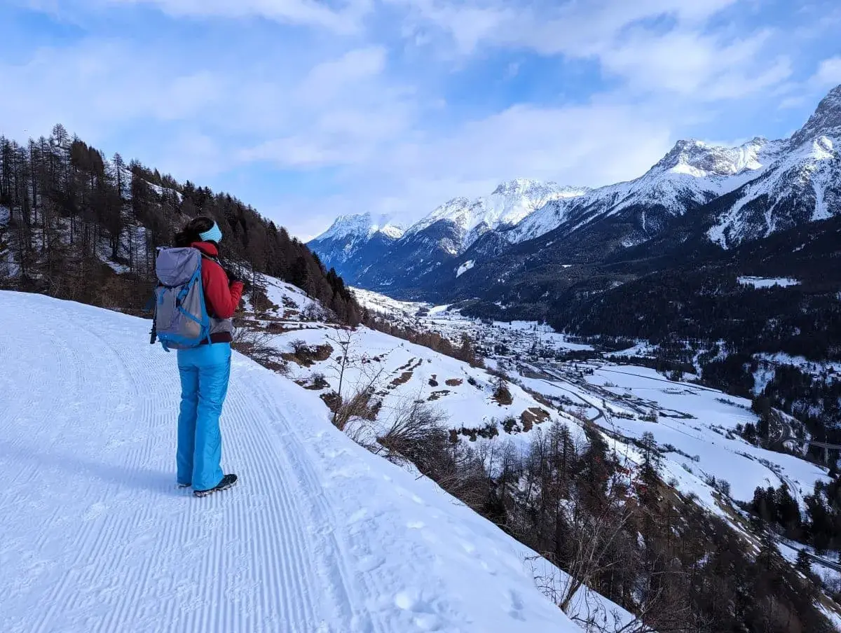 Linda steht auf dem Winterwanderweg Scuol nach Ftan und geniesst die Aussicht auf die verschneiten Gipfel in der Ferne