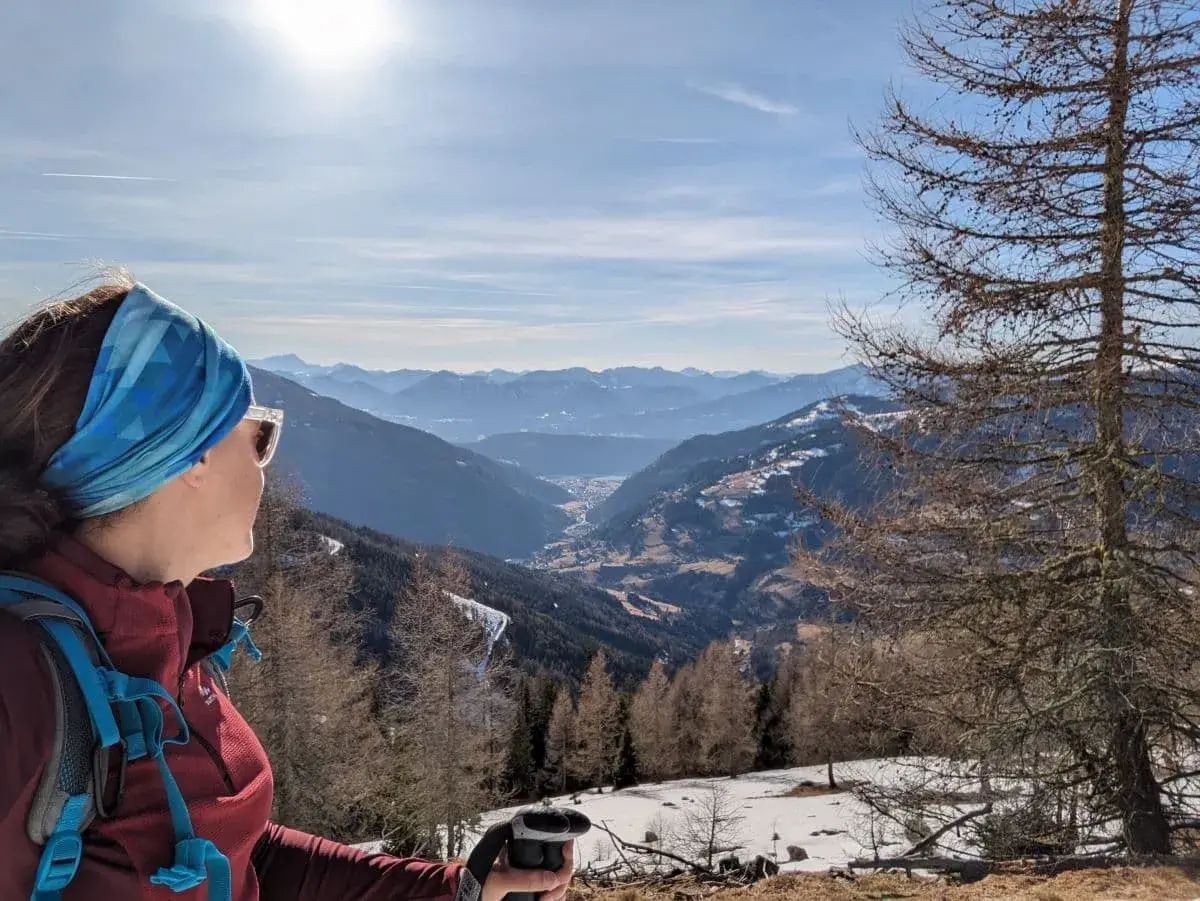 Linda guckt von der winterlichen Nockalm in die Ferne, wo man den Millstätters See in der Sonnen glänzen sehen kann