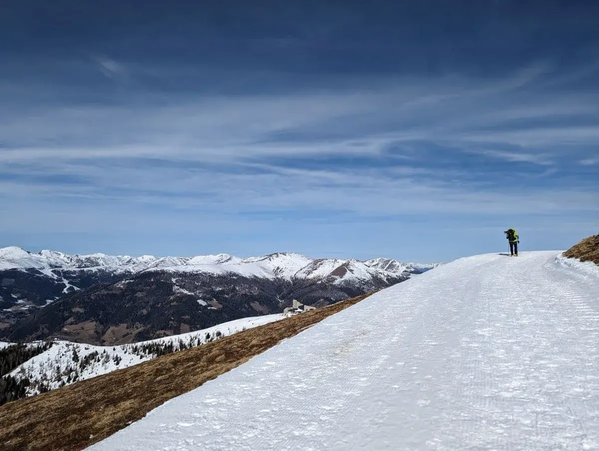 Einsamer Winterwanderer auf einem gespurten Winterwanderweg mit Blick auf verschneite Gipfel in der Ferne.