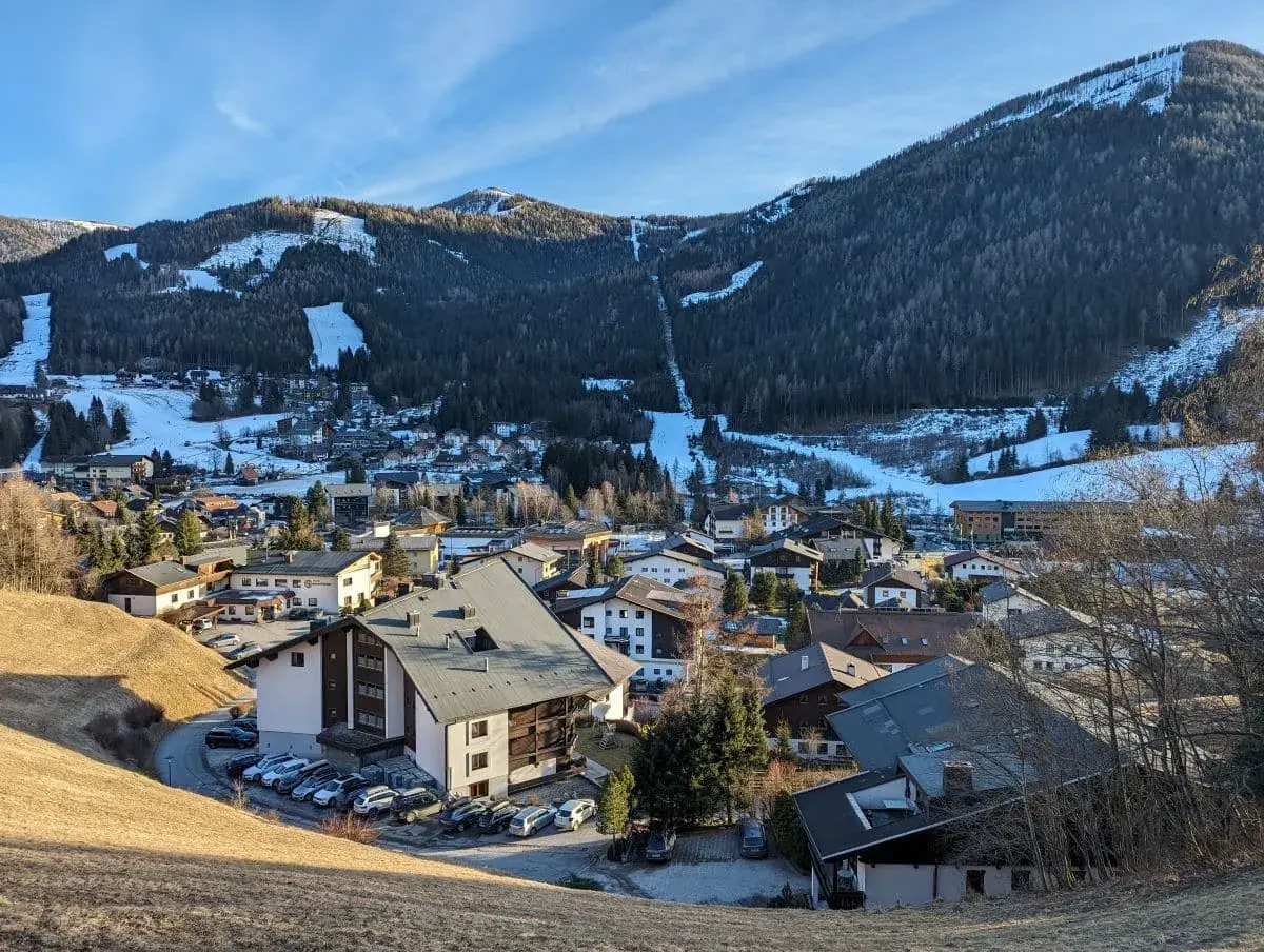 Viele Dorfhäuser von Bad Kleinkirchheim im Winter von oben. Die Skilifte der Nockberge und viel Wald an den Hängen im Hintergrund.