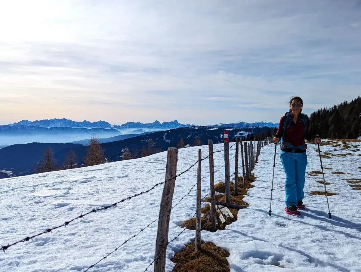 Linda wandert mit Schneeschuhen entlang eine aussichtsreichen Grats oberhalb von Bad Kleinkirchheim. Im Hintergrund die verschneiten Alpengipfel Österreichs