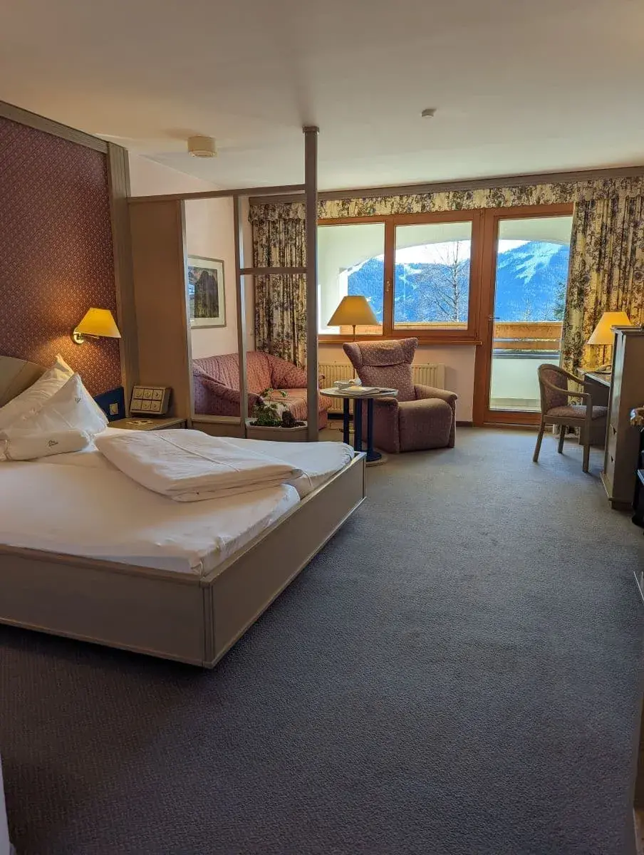 Mein Hotelzimmer im St. Oswald Hotel, mit Bett und tollem Ausblick durch die Fenster auf das winterliche Bad Kleinkirchheim