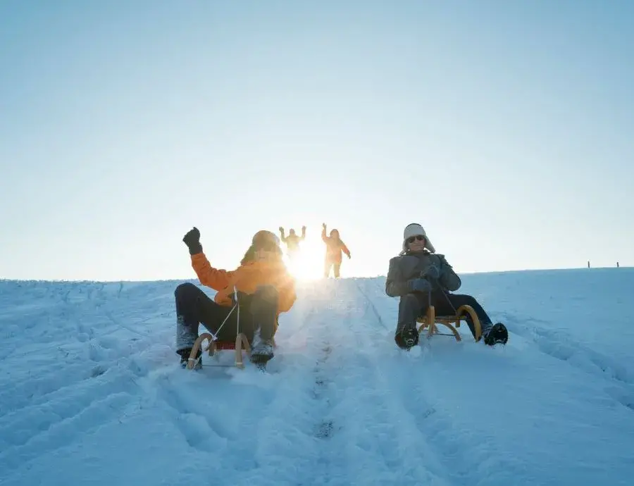 Linda und eine andere Personen rutschen auf Schlitten einen verschneiten Berg bei Bad Kleinkirchheim im Winter herunter.