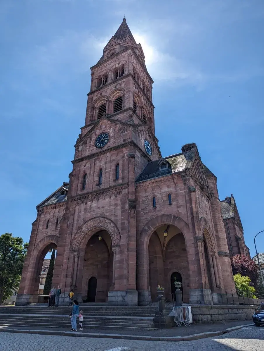 Die Kirche auf dem Marktplatz von Münster im Elsass. Die rote Sandsteinkirche erhebt sich majestätisch in den blauen Himmel.