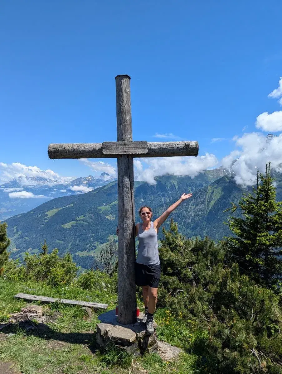 Linda steht freudestrahlend vor dem hölzernen Gipfelkreuz Croix de l'Aguille, einem Highlight beim Wandern in Champery