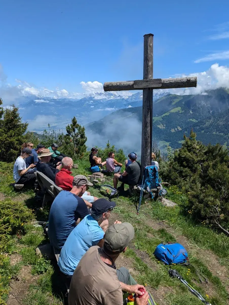 Eine Wandergruppe sitzt am Gipfelkreuz in Champery, macht Pause und genießt den Ausblick ins Val d'Illiez.
