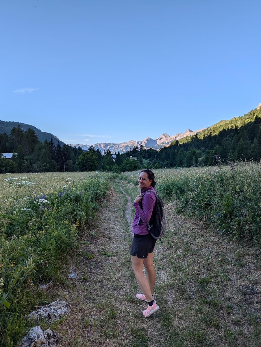 Linda wandert auf einem steinigen Pfad durch eine grüne Landschaft, sitzt auf einem Felsen und trägt einen Rucksack. Sie trägt die pinkfarbenen Barfußschuhe.