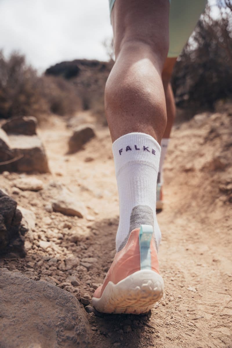 Eine Nahaufnahme von Lindas Füßen, die auf einem staubigen Wanderweg laufen. Auch hier sind die pinkfarbenen Primus Trail Knit Schuhe und weiße Socken von Falke gut zu erkennen.