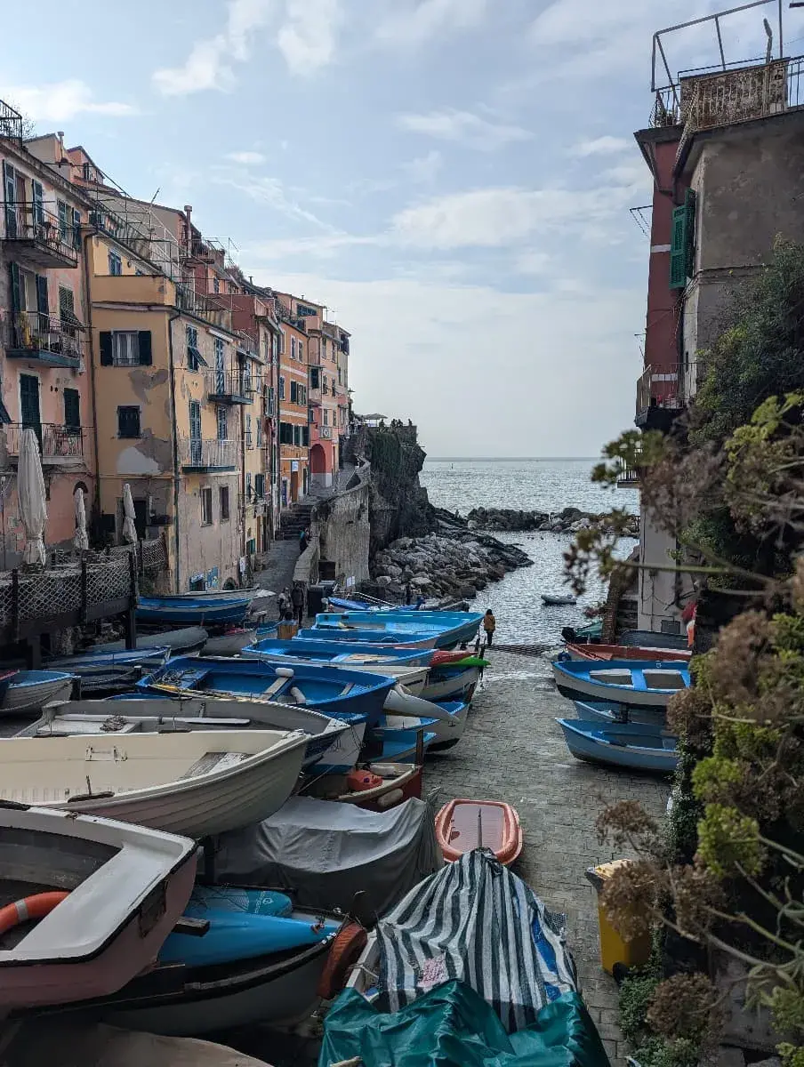 Eine enge Gasse in Riomaggiore führt zum Meer, gesäumt von bunten Fischerbooten und alten Gebäuden.