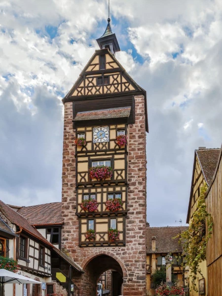 Das berühmte Dolder-Tor, ein historisches Wahrzeichen von Riquewihr, das zu den bedeutendsten Elsass Sehenswürdigkeiten gehört. Der mittelalterliche Torturm mit seiner markanten Fachwerkfassade und den farbenfrohen Blumenarrangements thront über einer gepflasterten Gasse und erinnert an die reiche Geschichte des Dorfes.