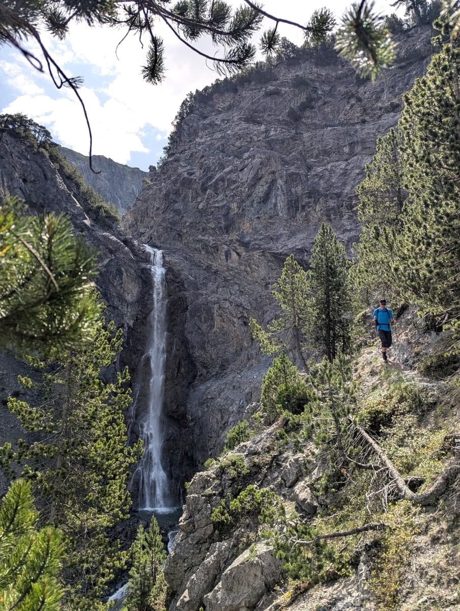 Ein Wanderer nähert sich dem imposanten Alteinfall bei Arosa, der sich über steile Felswände in die Tiefe stürzt und von Kiefernwald umrahmt ist. Diese spektakuläre Naturkulisse ist ein Highlight beim Wandern in Arosa.