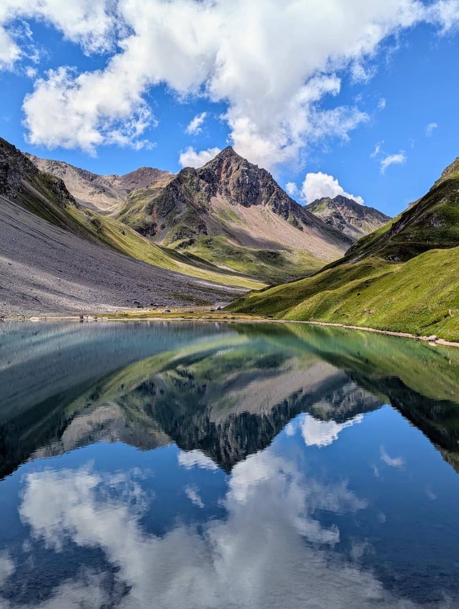 Kristallklarer Bergsee mit Spiegelung der umliegenden Gipfel und einer dramatischen Wolkenkulisse. Ein Highlight beim Wandern in Arosa.