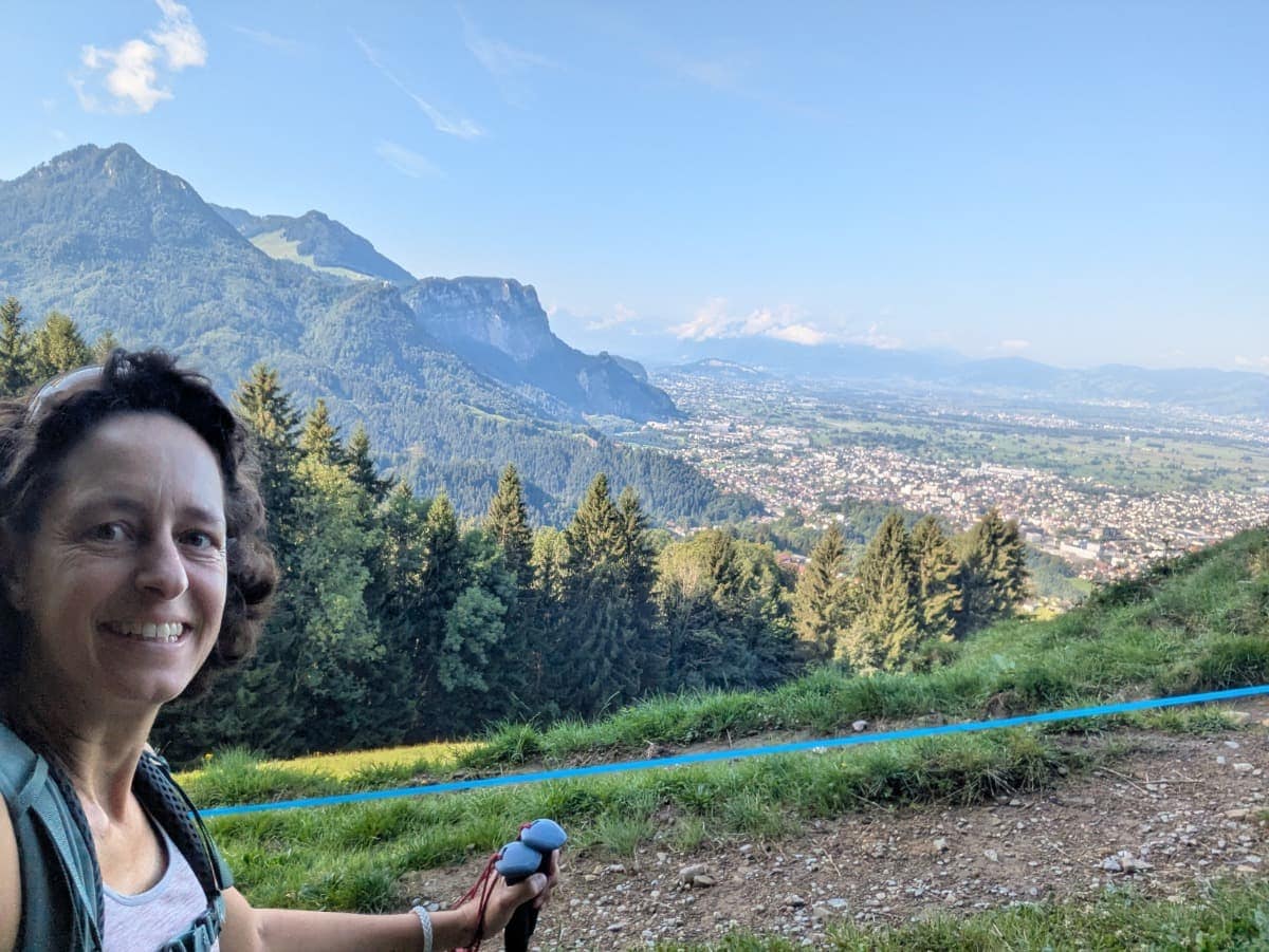 Selfie von Linda beim Wandern über grüne Wiesen unweit der Alpe Schwende, mit Blick über das Rheintal und die umliegenden Berge in Vorarlberg. Dornbirn in Vorarlberg ist ideal für Panorama-Ausblicke wie diesen.
