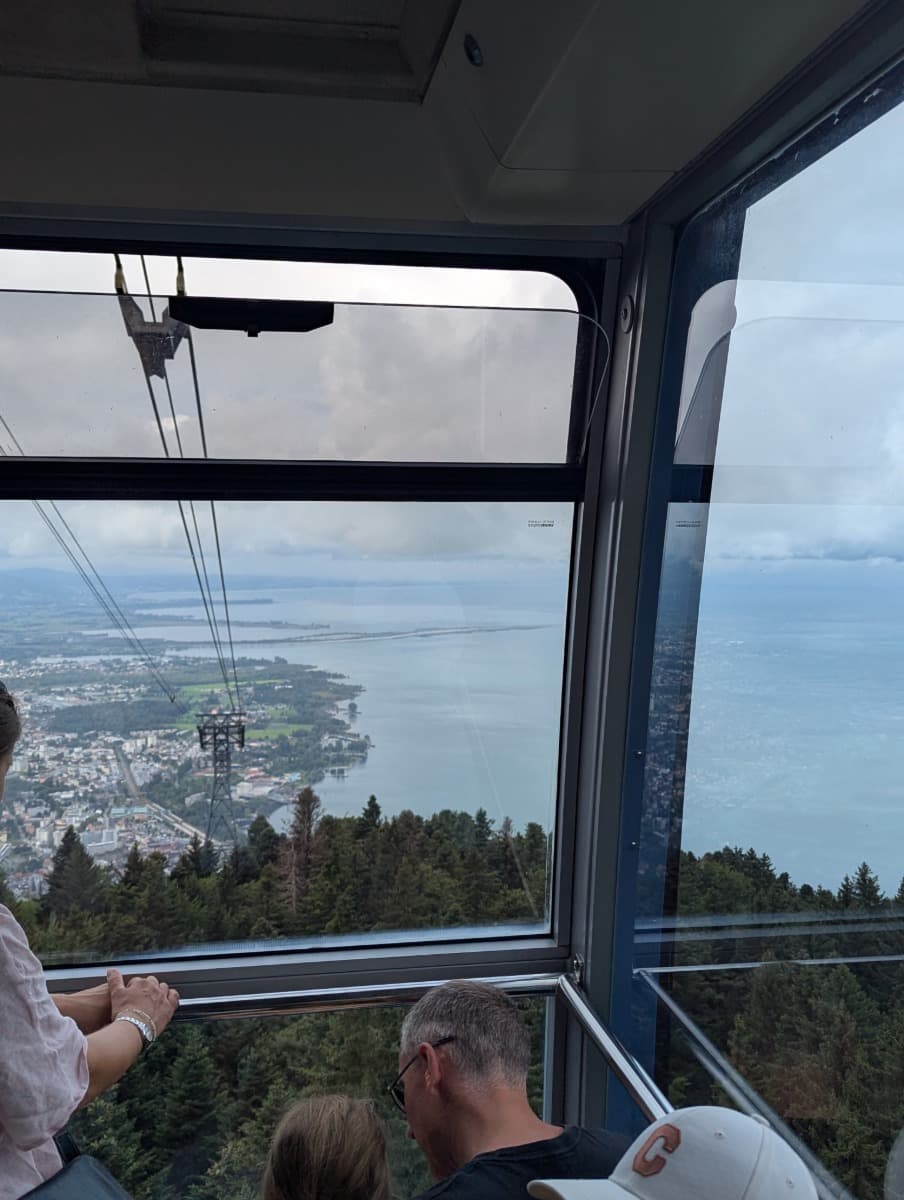 Blick aus einer gläsernen Seilbahngondel auf Wälder, Stadt und Bodensee in der Ferne. Die Fahrt zur Pfänder-Bergstation ist ein tolles Ausflugsziel während eines Kurztrips in Dornbirn in Vorarlberg.