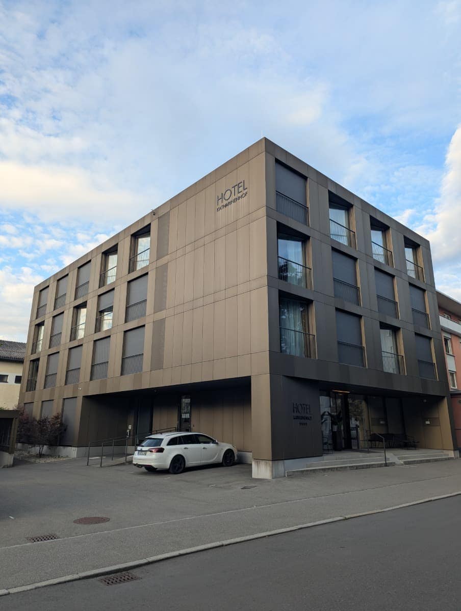 Modernes Hotelgebäude in Bronzeoptik mit schlichtem Schriftzug „Hotel Katharinenhof“, davor ein weißer Kombi. Zentral gelegen ist dieses Hotel ein guter Ausgangspunkt für einen Dornbirn Kurztrip.