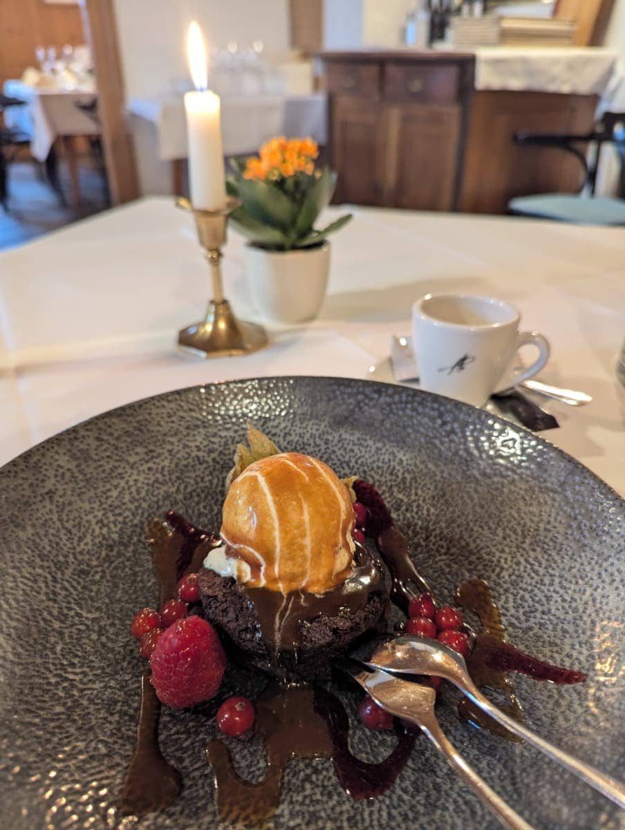 Ein kunstvoll angerichtetes Dessert mit Vanilleeis auf Schokokuchen, garniert mit Beeren, steht auf einem gedeckten Tisch mit Kerze und Espresso. Kulinarik darf beim Dornbirn Kurztrip natürlich nicht fehlen.