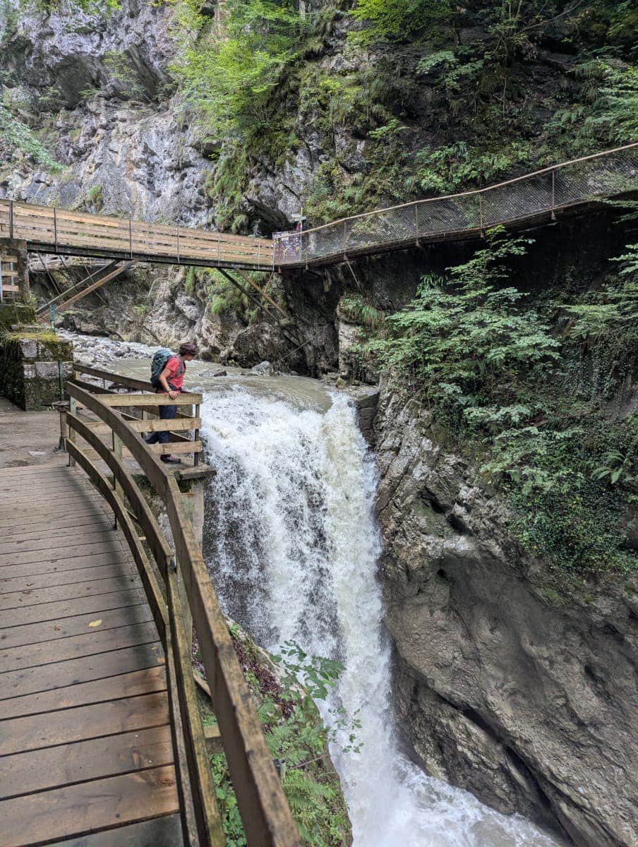 Linda lehnt über einem Geländer in der Rappenlochschlucht direkt neben einem tosenden Wasserfall, umgeben von Holzstegen und steilen Felswänden. Diese Wanderung gehört zu den Highlights eines Dornbirn Kurztrips.