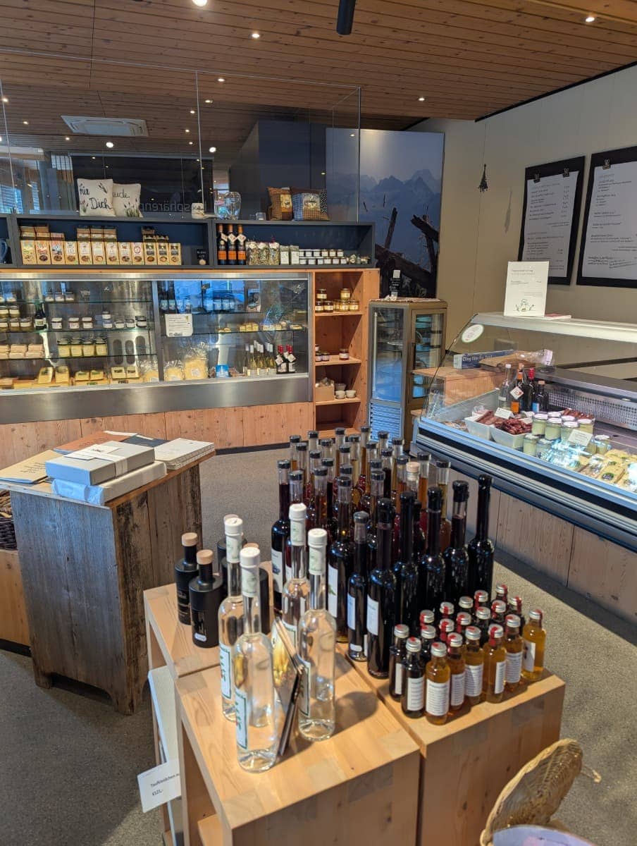Hofladen-Atmosphäre mit Holzregalen und einer Auswahl an Edelbränden, Käse, Honig und Kräuterprodukten aus der Region. Der Verkaufsraum im biosphärenpark.haus spiegelt die Vielfalt lokaler Erzeugnisse aus dem Großen Walsertal wider.