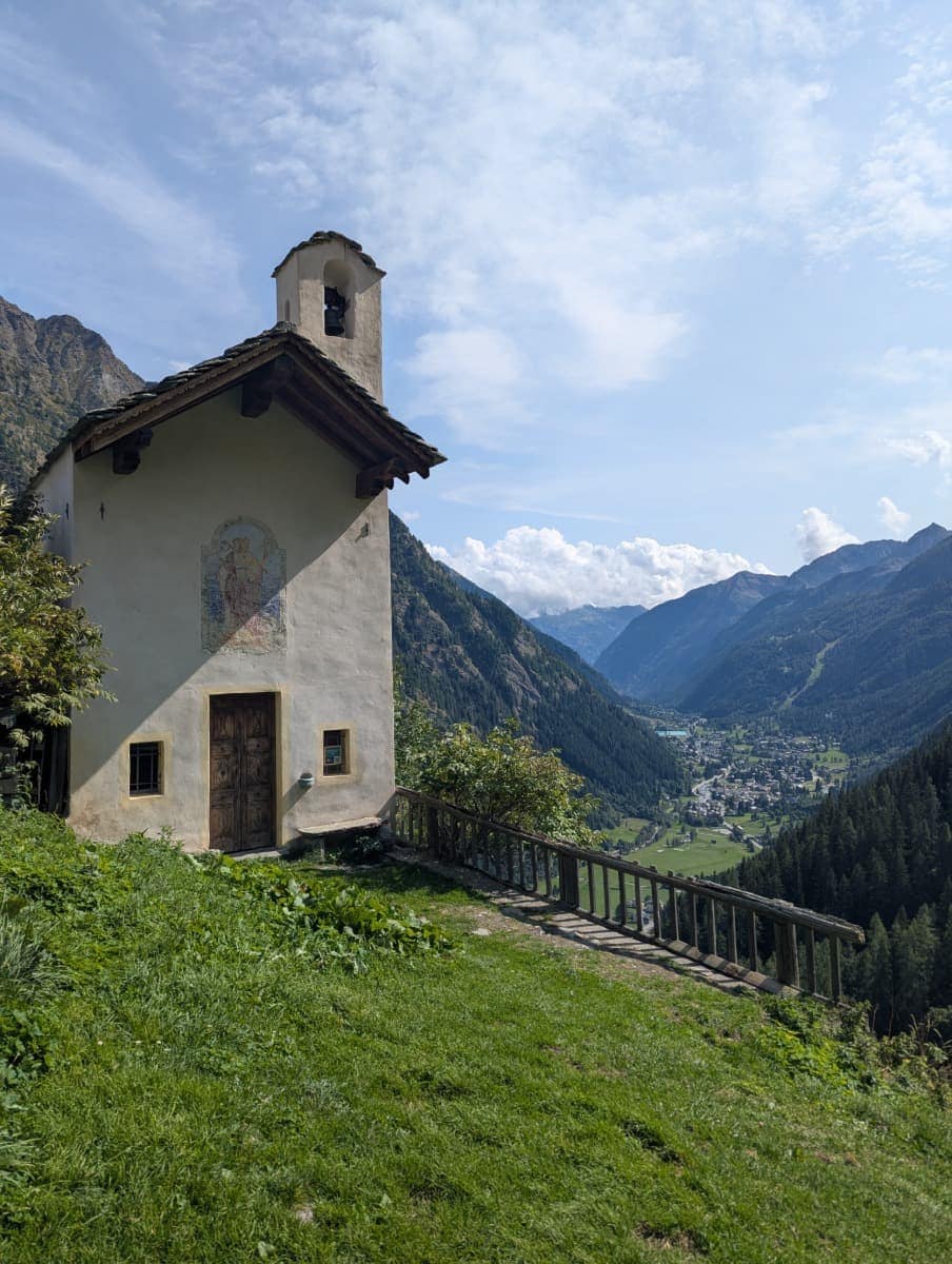 Eine kleine Kapelle mit Wandmalerei steht am Hang des Weilers Alpenzu oberhalb von Gressoney und überblickt das Tal. Sie ist ein stiller Aussichtspunkt und verbindet Kultur mit Natur im Aostatal.