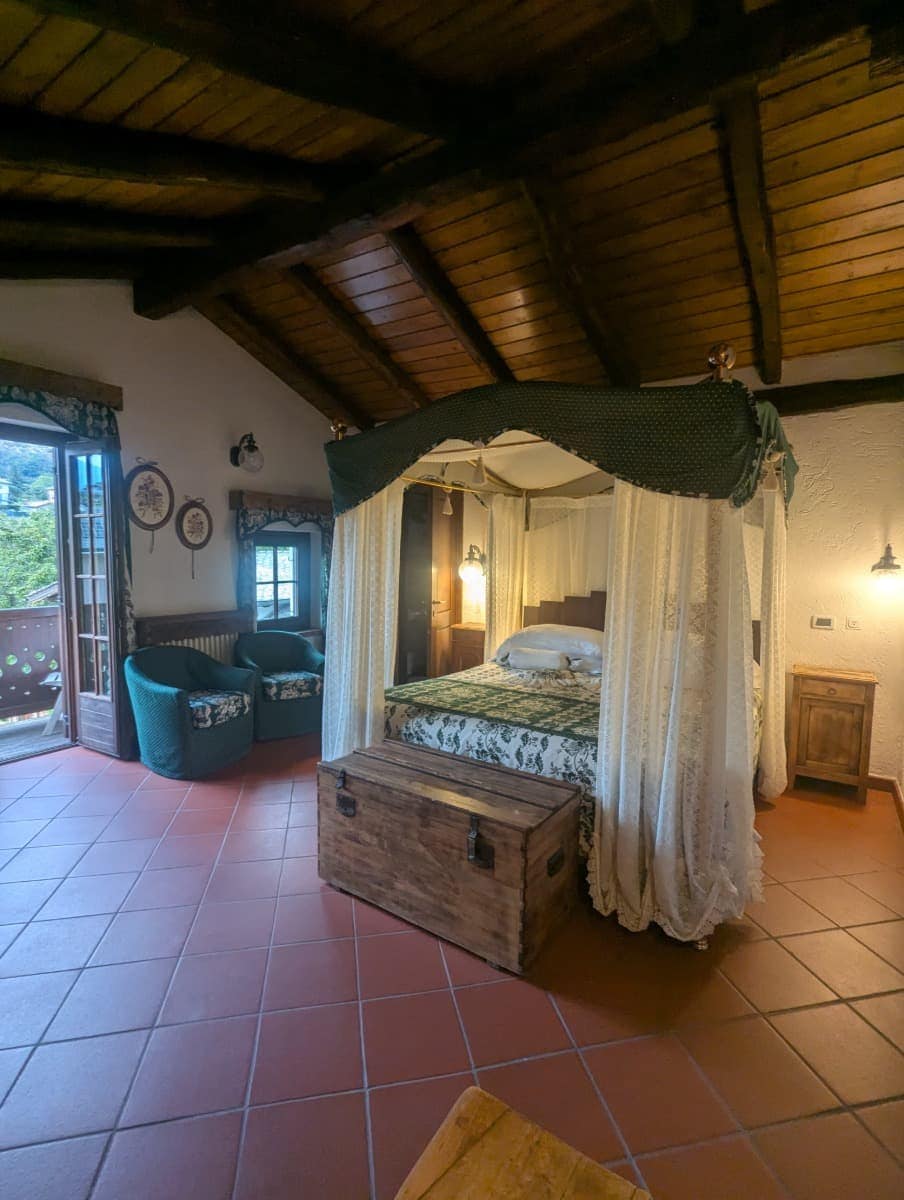 Ein gemütliches Zimmer mit Himmelbett, rustikalem Holzbalken-Dach und Balkonblick strahlt alpine Behaglichkeit aus. Solche Unterkünfte stehen für den Charme der Hotellerie im Aostatal.
