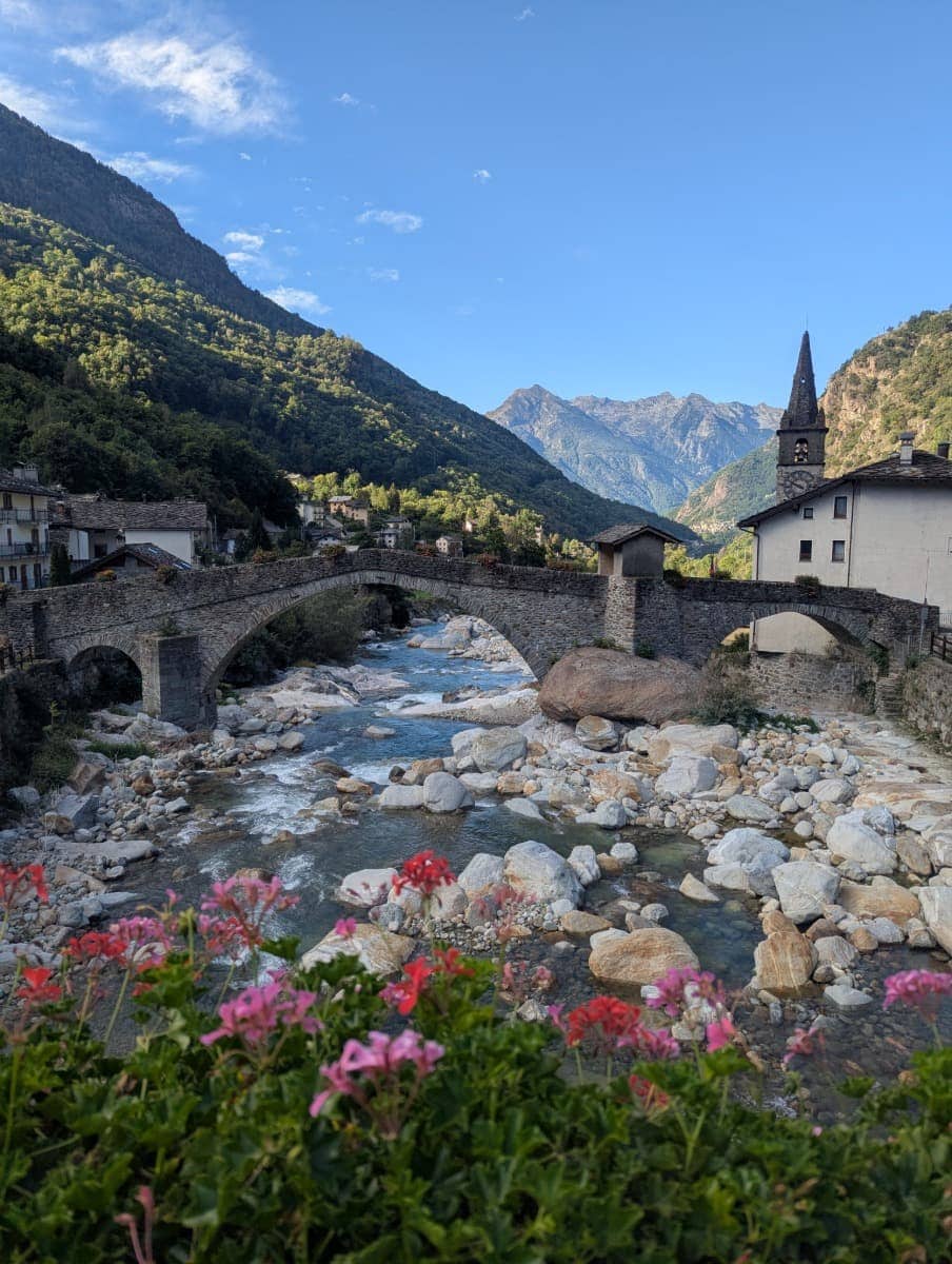Die Römerbrücke von Lillianes spannt sich in einem eleganten Bogen über die Lys, eingerahmt von alten Häusern und den Bergen des Aostatals. 