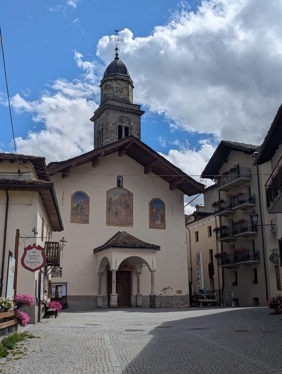 Die Pfarrkirche von Cogne mit ihrem markanten Glockenturm und den Fresken an der Fassade prägt das Ortszentrum. Sie ist ein kulturelles Wahrzeichen und verleiht dem Dorf im Aostatal historischen Charme.