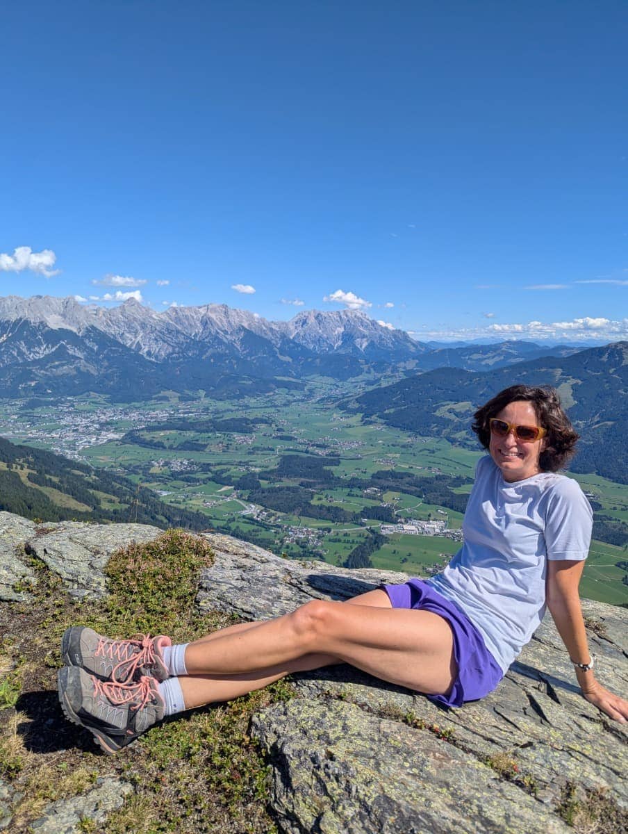 Linda entspannt auf einem Felsen mit weitem Blick über das Tal Richtung Saalfelden und das Steinerne Meer. Das Bild vermittelt die Ruhe und Weite des Saalachtaler Höhenwegs.