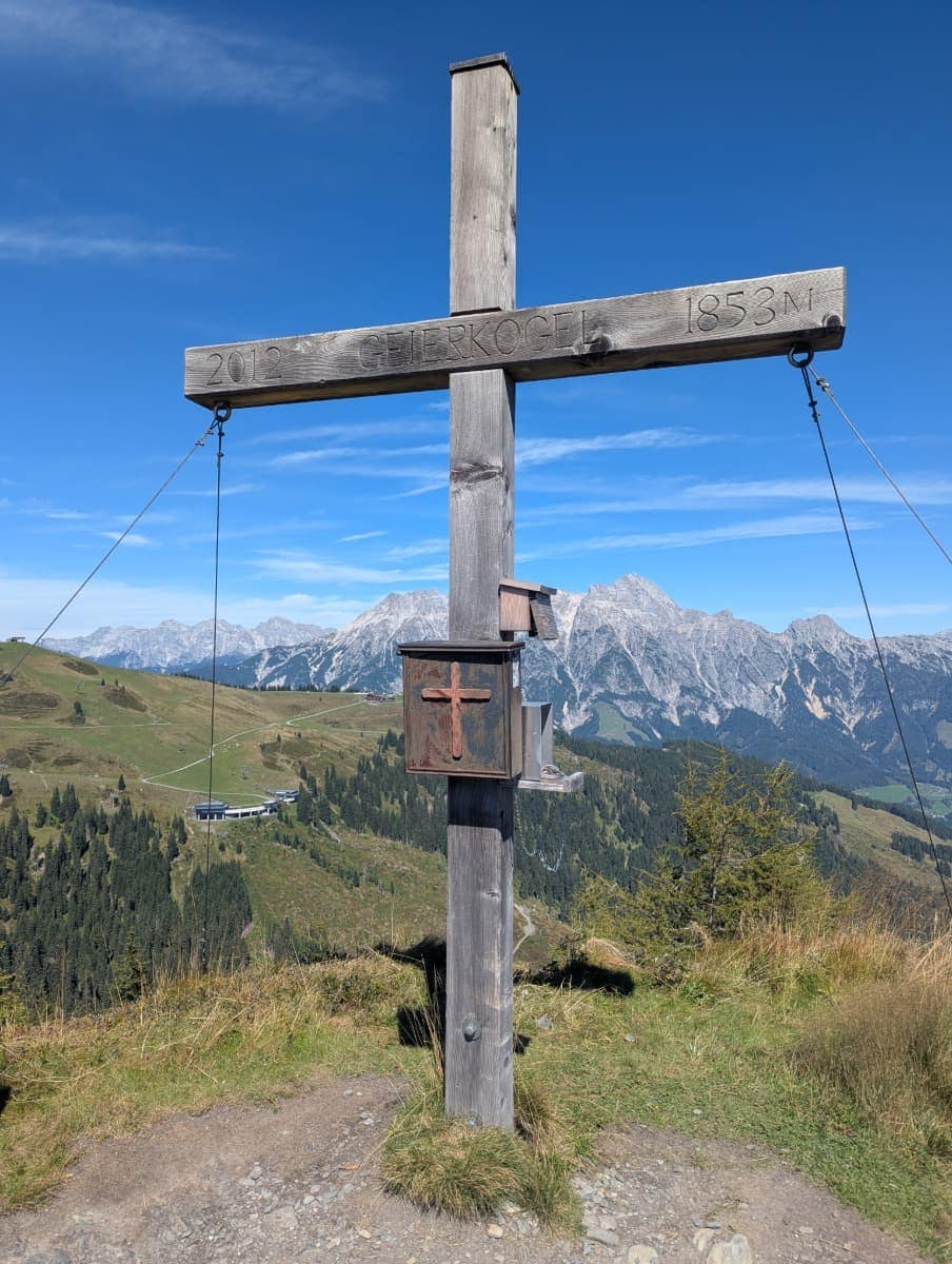 Gipfelkreuz am Geierkogel auf 1853 Metern mit markantem Blick ins Tal und auf die Leoganger Steinberge. Dieses Bild symbolisiert die alpinen Höhepunkte der Wanderung im Glemmtal