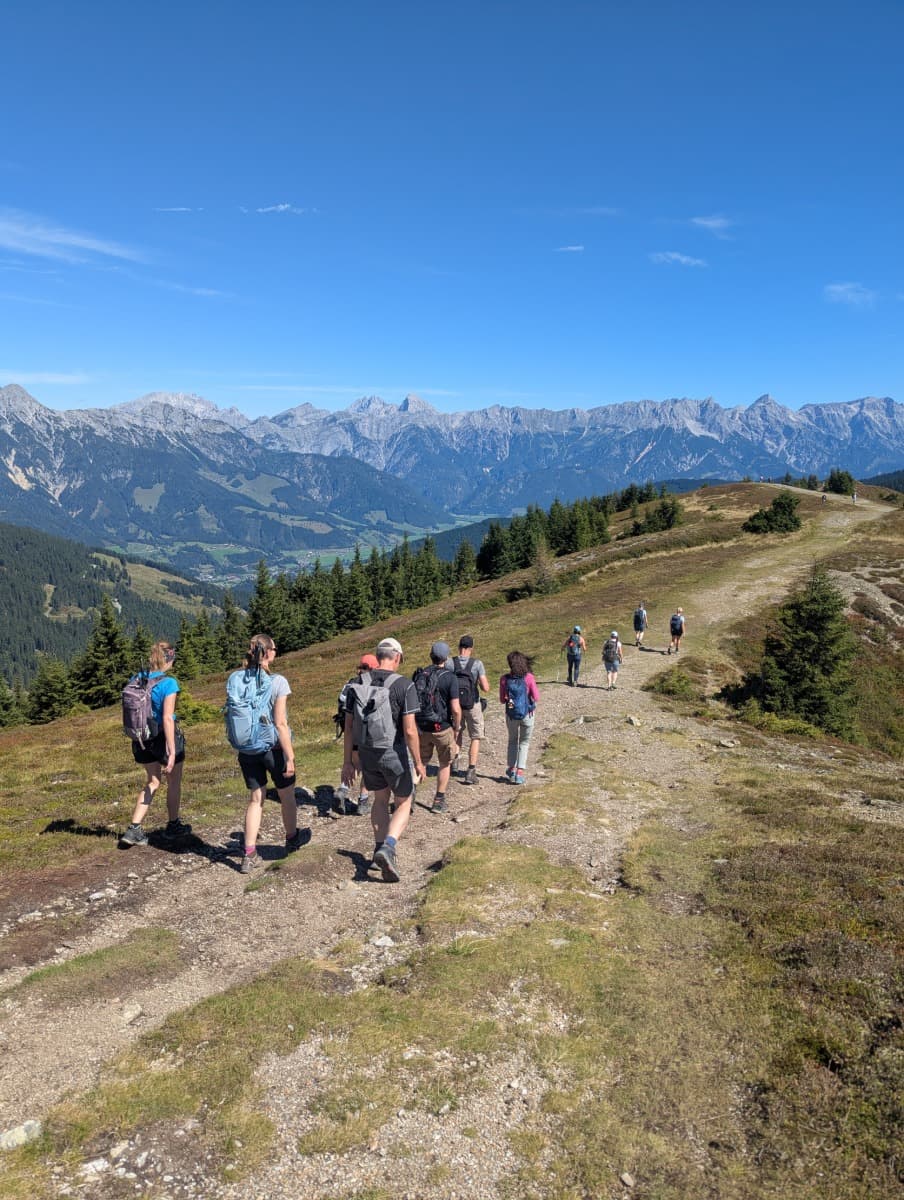 Eine Gruppe Wanderer folgt dem Höhenweg über einen sanften Kamm mit Blick auf das Steinerne Meer und den Hochkönig. Das Bild verdeutlicht die Panorama-Abschnitte des Saalachtaler Höhenwegs.