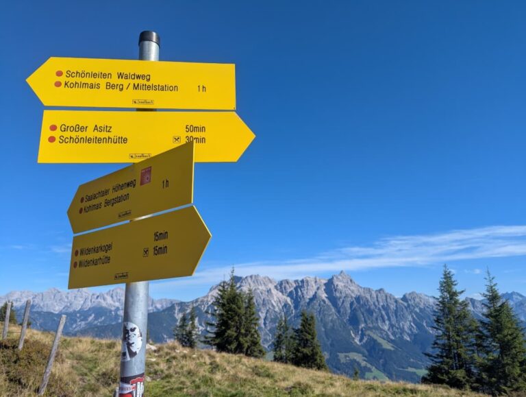 Gelbe Wegweiser markieren Abzweigungen zu Schönleitenhütte, Großem Asitz und Saalachtaler Höhenweg. Das Bild zeigt die gute Beschilderung und Orientierungsmöglichkeiten des Saalachtaler Höhenweg