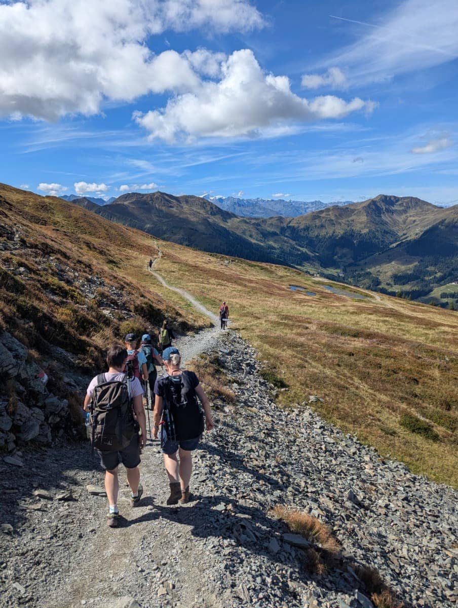 Gruppe von Wanderern auf dem Pinzgauer Spaziergang bei Saalbach Hinterglemm. Der aussichtsreiche Höhenweg führt über weite Almwiesen mit Blick auf die Alpenlandschaft.